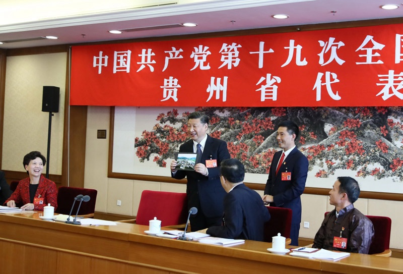 10月19日，習(xí)近平同志參加黨的十九大貴州省代表團討論。這是遵義市播州區(qū)花茂村黨總支書記潘克剛將一幅鳥瞰村子新貌的照片送到習(xí)近平面前。習(xí)近平起身接過照片，邊看邊稱贊：“這是風(fēng)景畫，很漂亮！”新華社記者 蘭紅光 攝