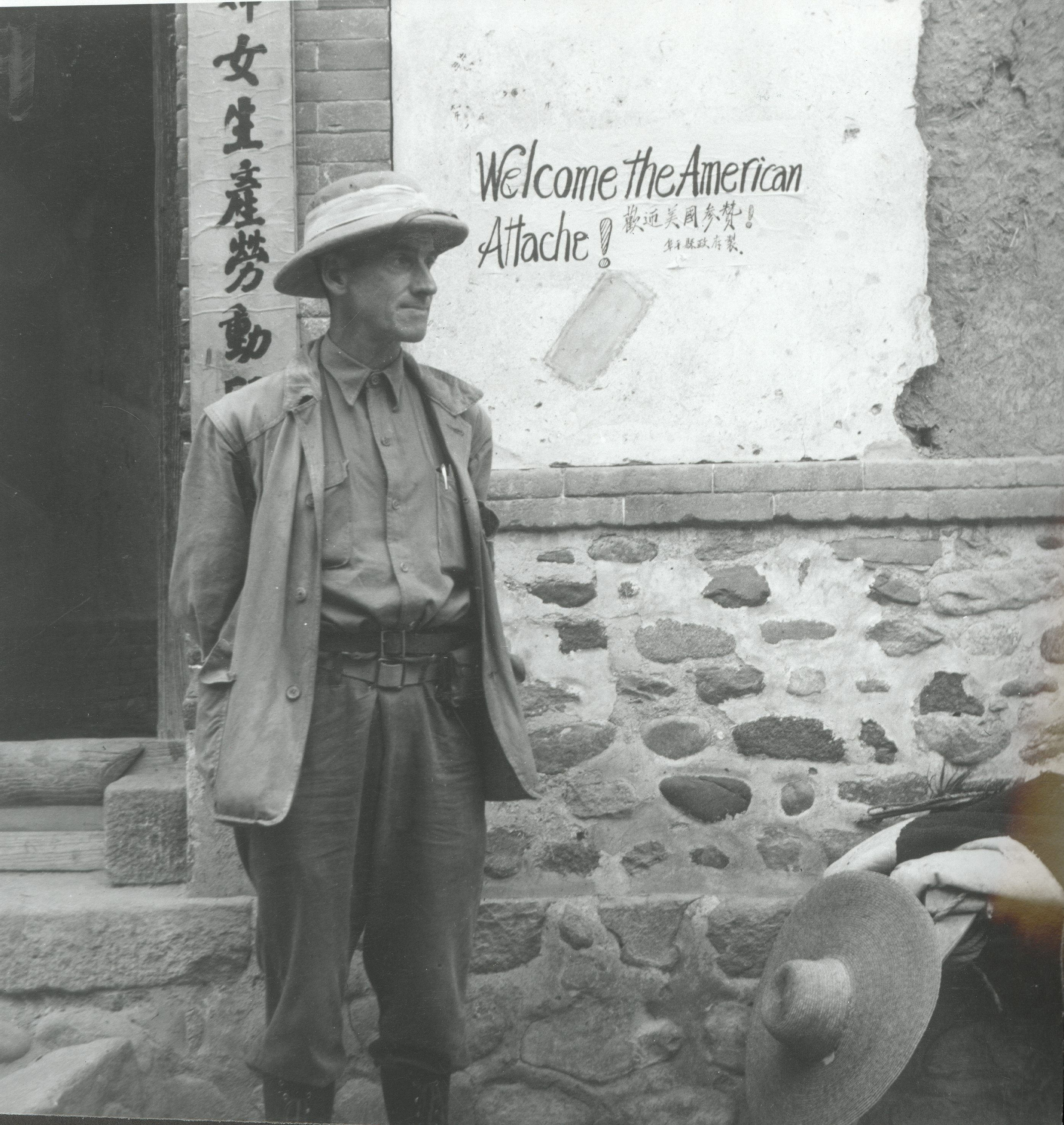 卡爾遜在河北阜平，他身后的墻上用中英文寫著：“歡迎美國參贊?！?></p>
<p style=